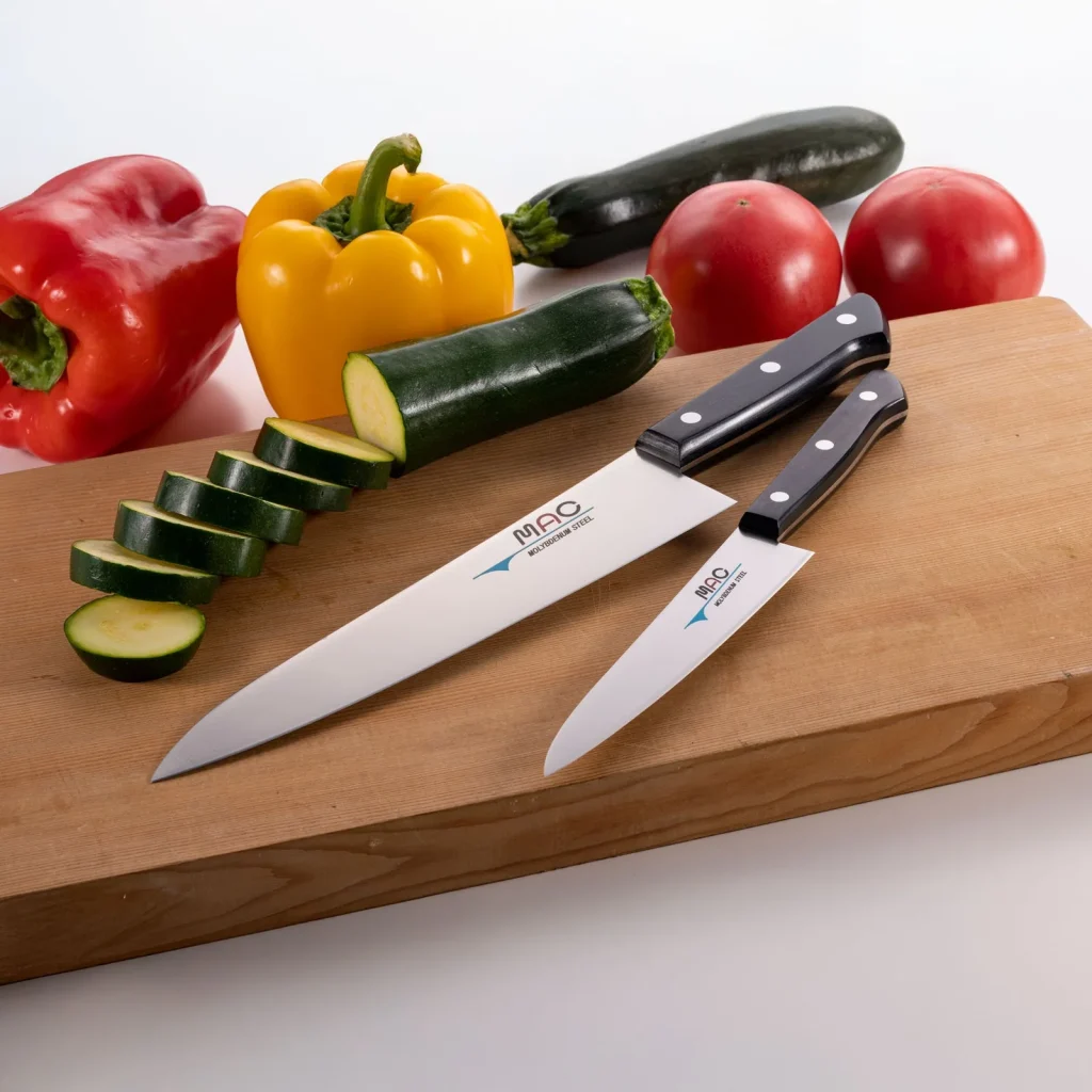 To kniver fra MAC Chef-serien på en trefjøl med paprika, tomater og oppskåret agurk.