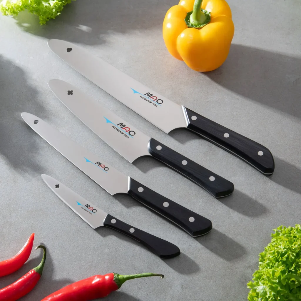 Fire kniver fra MAC Original-serien på grå benk, med gul paprika, chili og salat rundt.