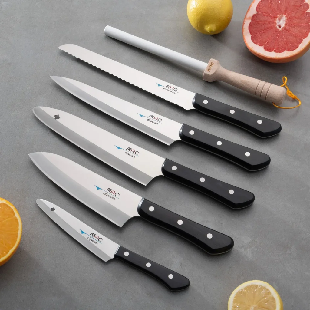Fem kniver og en slipestav fra MAC Superior-serien på grå flate, med sitron, appelsin og grapefrukt rundt.